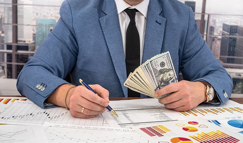 An EB5 investor working on an existing business plan while holding a stack of dollars.