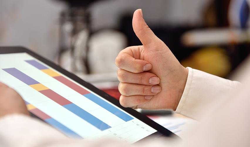 A hand giving a thumbs up in front of a screen with immigrant investor capital graphs on it.