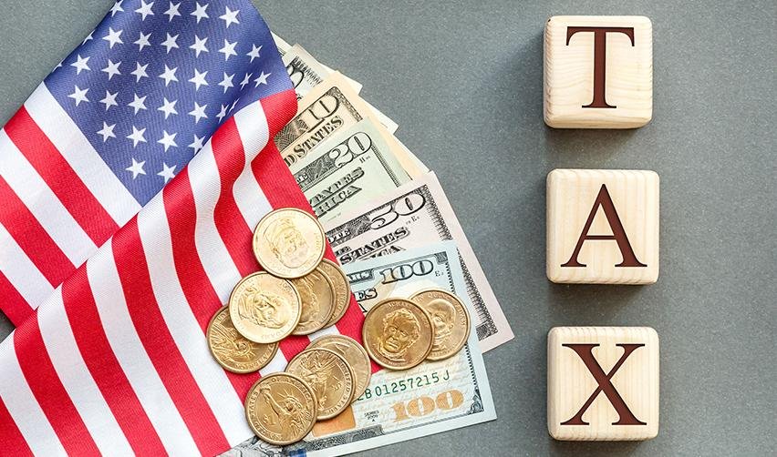 EB-5 capital investment money on top of an American flag and wooden blocks spelling out tax.