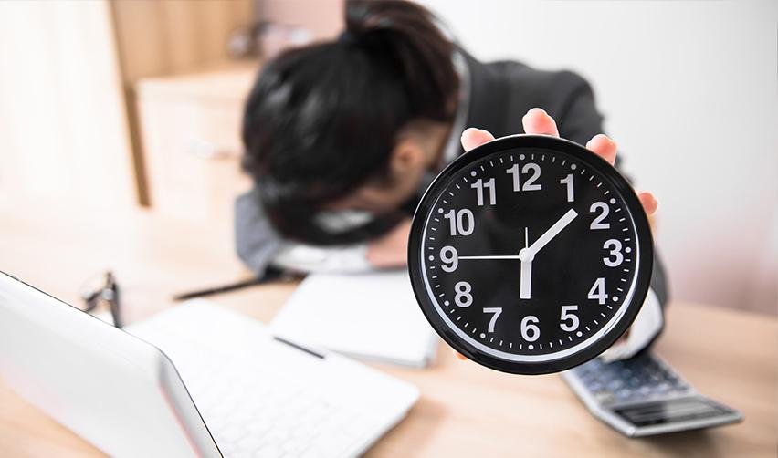 A distressed person with her head on her desk, holding a clock up to the camera, symbolizing immigrant investors frustrated with processing times.
