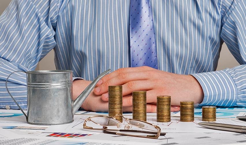 A person sitting at a desk with stacked coins and investment graphs on it.