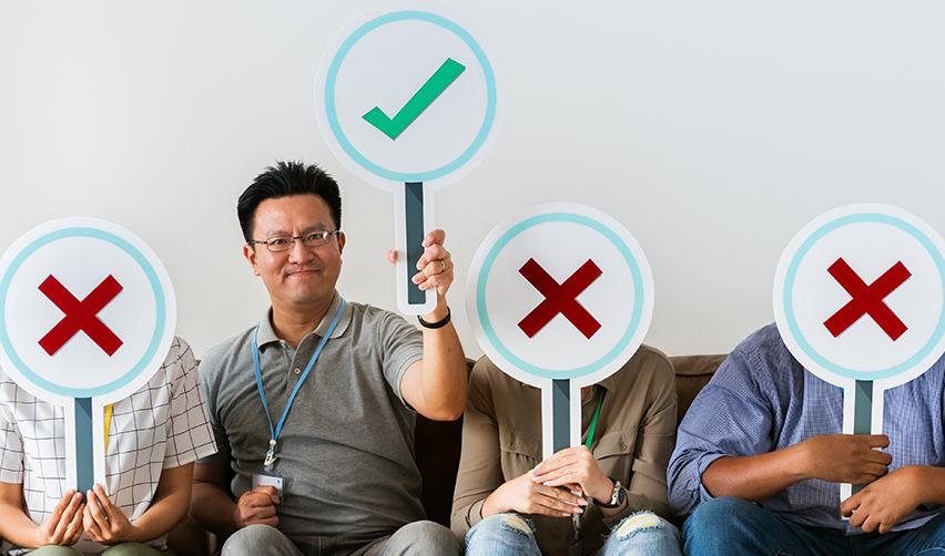 A person holding up a green check sign while others are sitting next to him with red cross signs on their faces. It symbolizes EB5 visa eligibility and who qualifies as an EB5 investor.