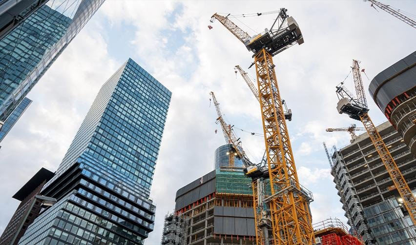 A city skyline with multiple high-rise buildings under construction, surrounded by yellow cranes. EB5 investment capital plays a key role in funding real estate developments, revitalizing urban areas, and generating jobs.