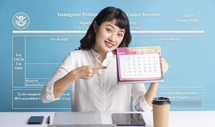 Smiling woman pointing to a calendar date in front of a Form I-526E backdrop, highlighting how EB5 timelines are tied to each fiscal year.