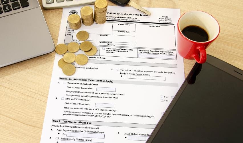 A stack of coins and a coffee mug on top of a USCIS petition form, representing the role of regional centers in the EB5 process.