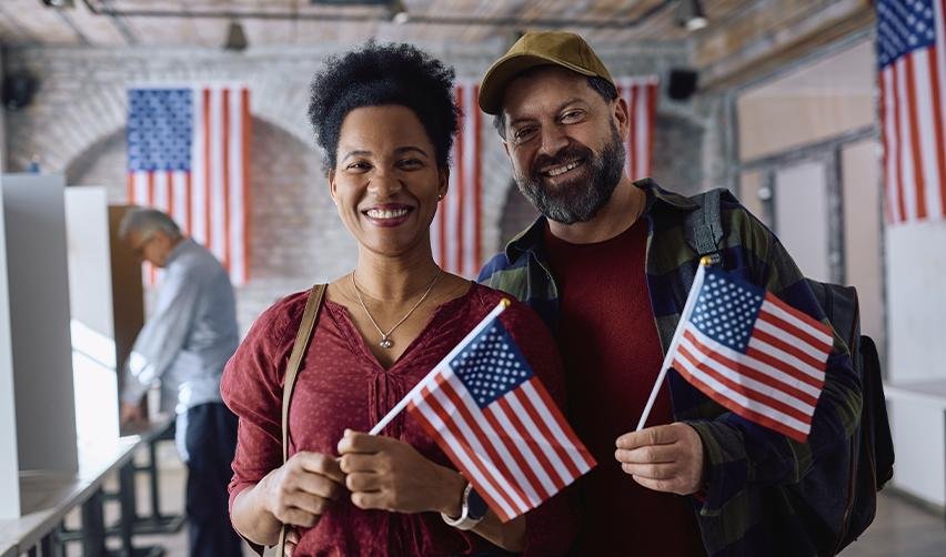 Couple smiling and holding American flags in a citizenship ceremony, symbolizing the benefits of immigrant visas and Green Card pathways.