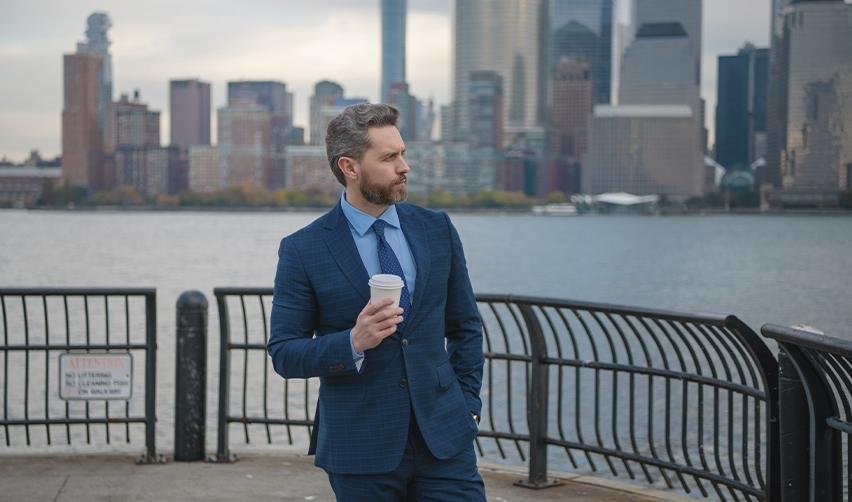 A Canadian citizen in a suit standing by a waterfront with a city skyline in the background. Illustrates the success of Canadian investors and entrepreneurs leveraging the EB5 immigration process for U.S. green card acquisition.