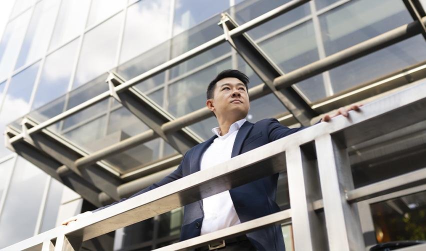 Confident businessman in a suit standing outside a modern office building, looking ahead. The security and long-term benefits of the EB5 visa as a direct path to U.S. residency.