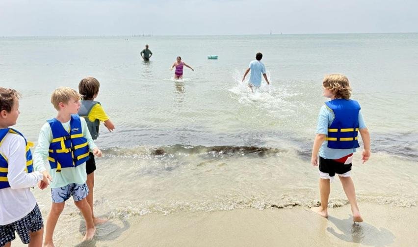 Children in life jackets enjoying summer activities on Bay Creek’s shoreline, highlighting family-friendly amenities that strengthen community appeal.