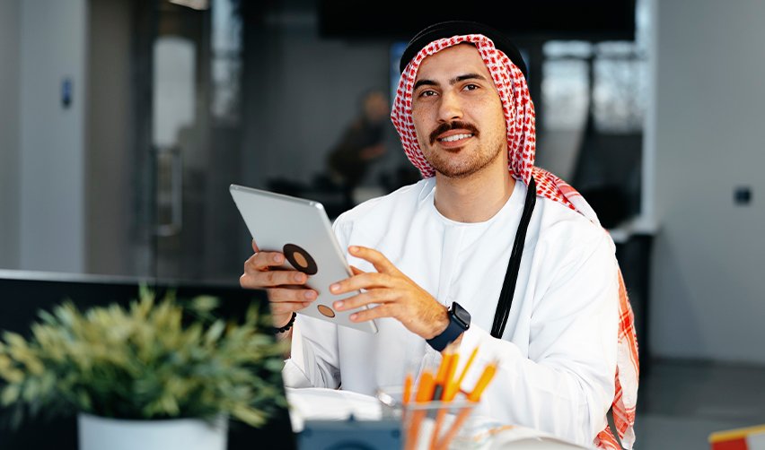 Middle Eastern businessman in traditional Gulf attire using a tablet in an office, representing Middle Eastern EB5 investors seeking fast U.S. green card options during regional instability.